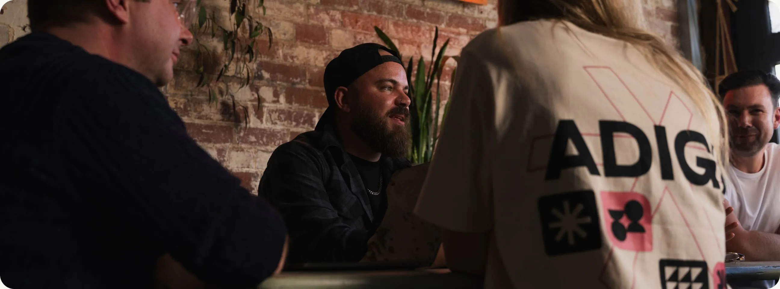 The team talking around a table in the studio, one of them in an Adigi T-shirt