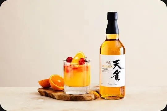 A bottle of Tenjaku whisky beside a cocktail garnished with orange
