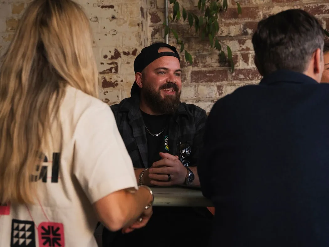 Three of the team talking and laughing around a table by a brick wall