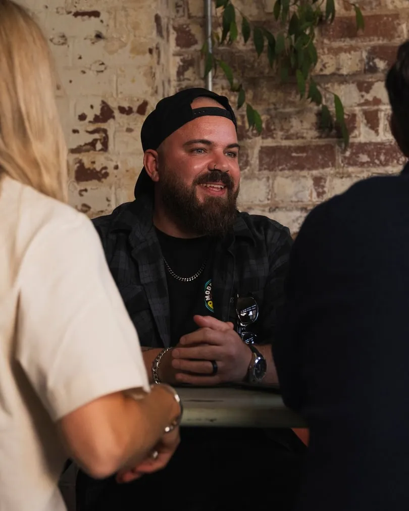 Three of the team talking and laughing around a table by a brick wall