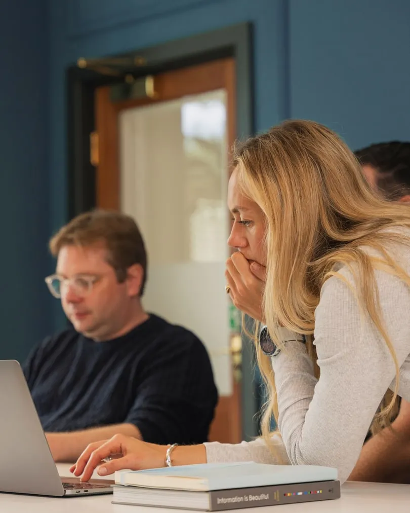 Two of the team leaning over a laptop together in the studio