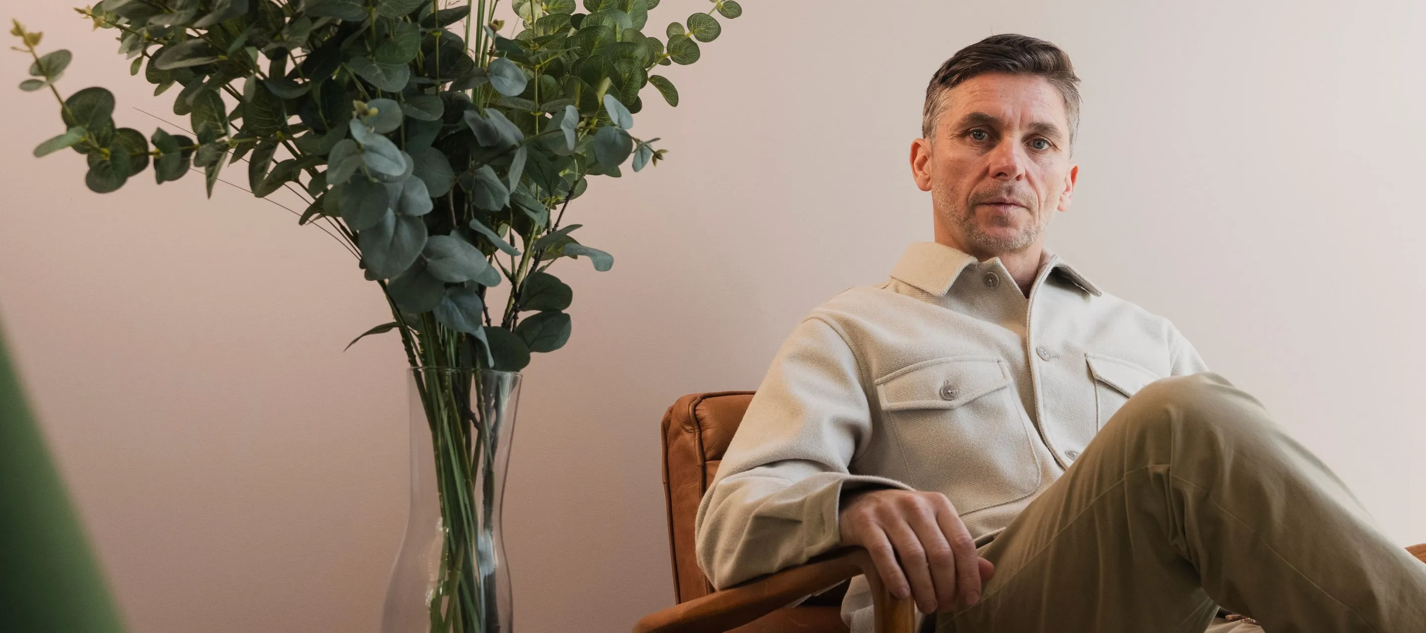 Dan Martin sitting in a leather chair beside a vase of eucalyptus