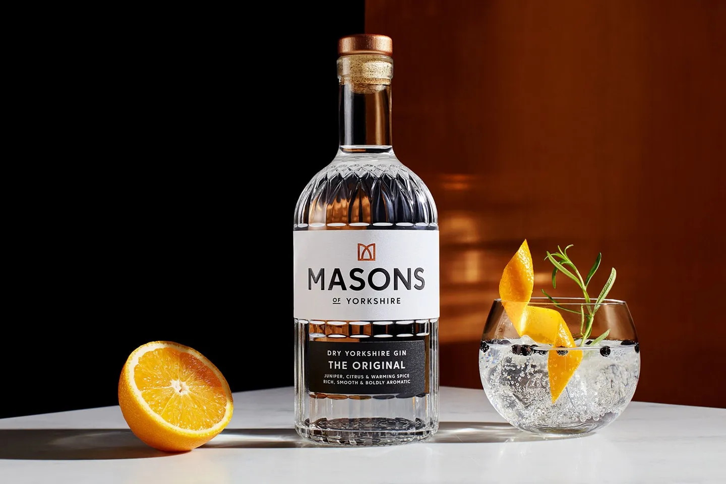 A bottle of Masons gin beside a gin and tonic and half an orange
