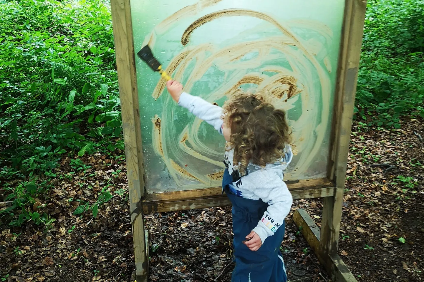 A child painting on a large canvas in the woods at Born of the Forest