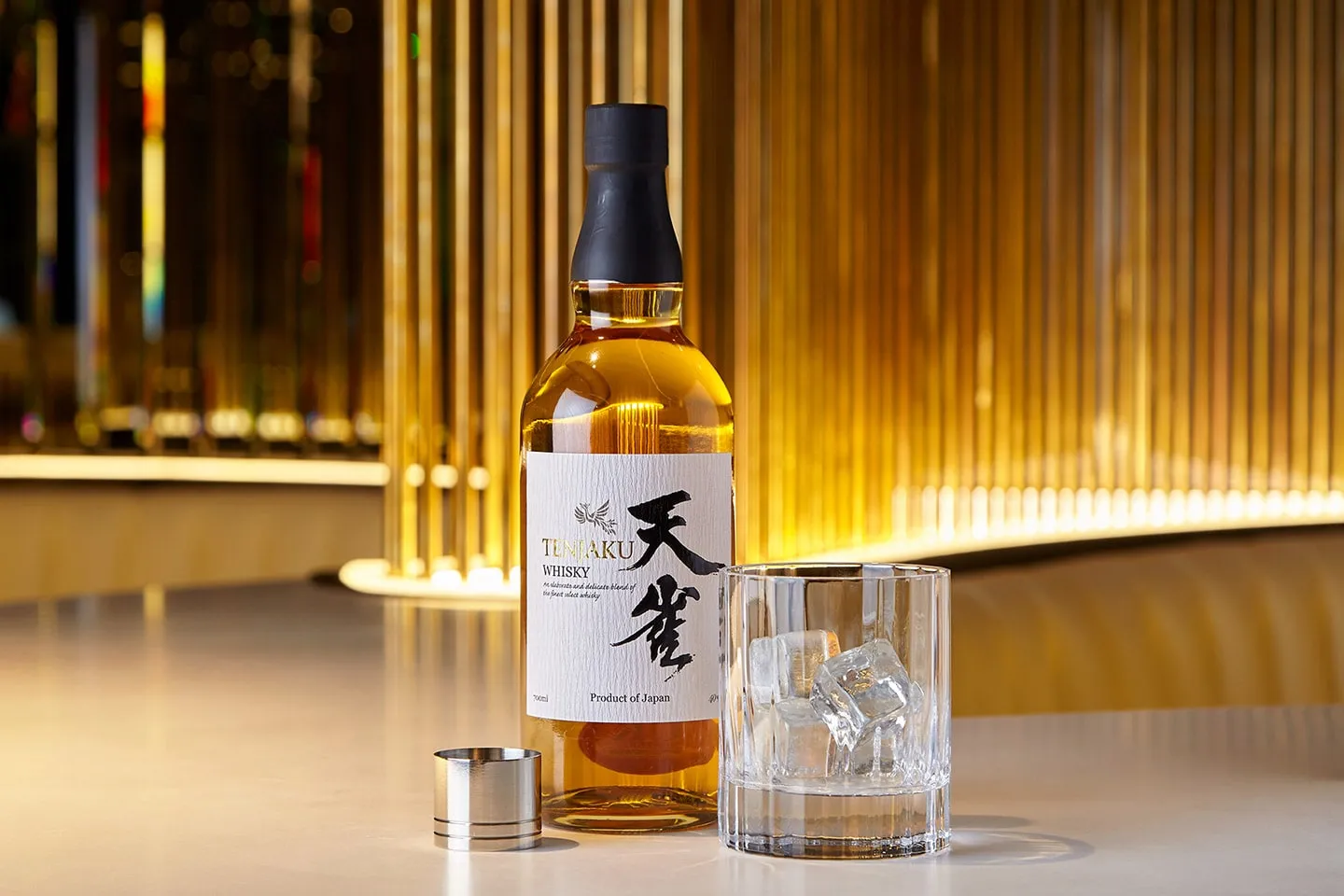 A bottle of Tenjaku whisky and a glass on a bar lit in gold