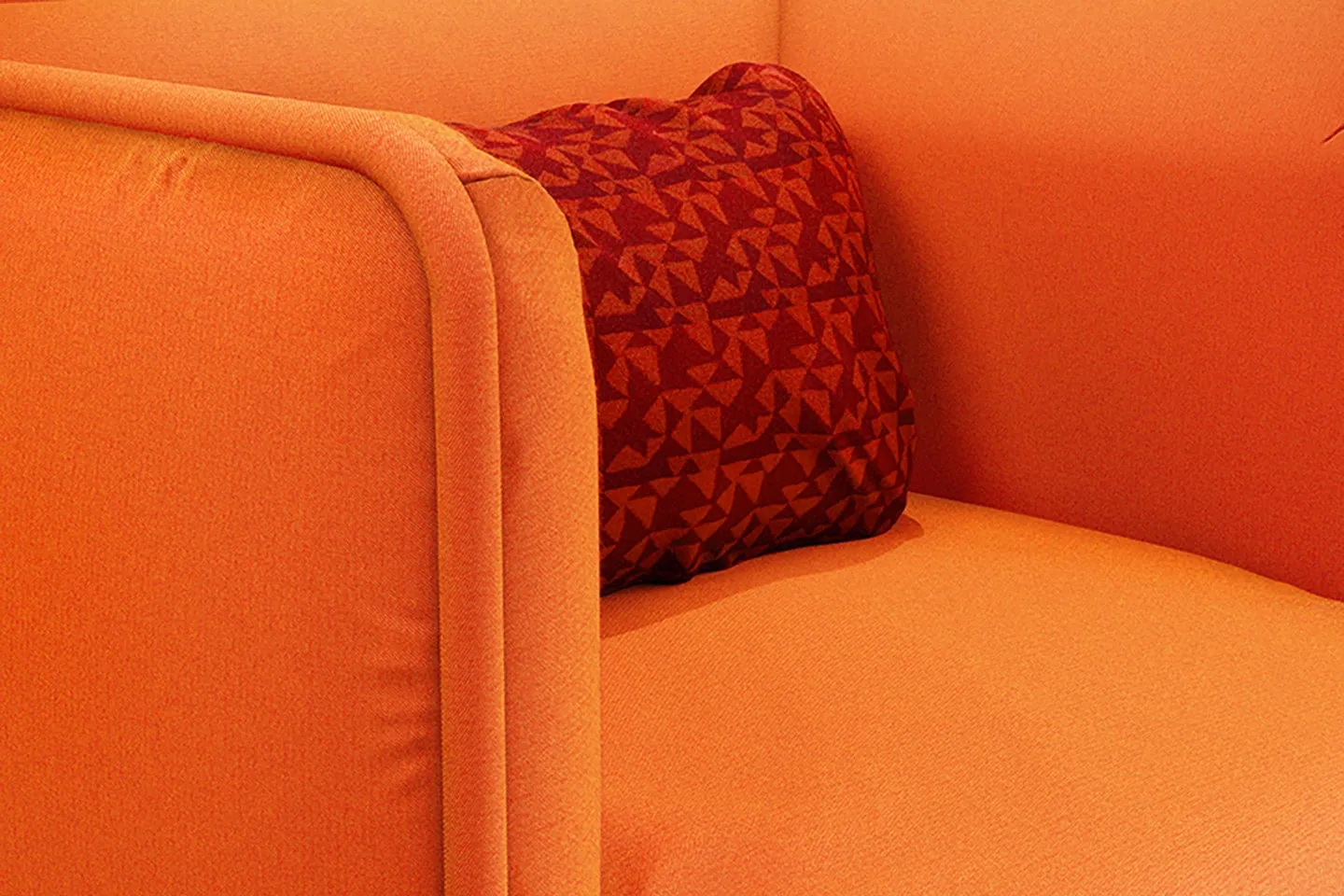 An orange upholstered sofa with a red patterned cushion in TextileMania fabrics