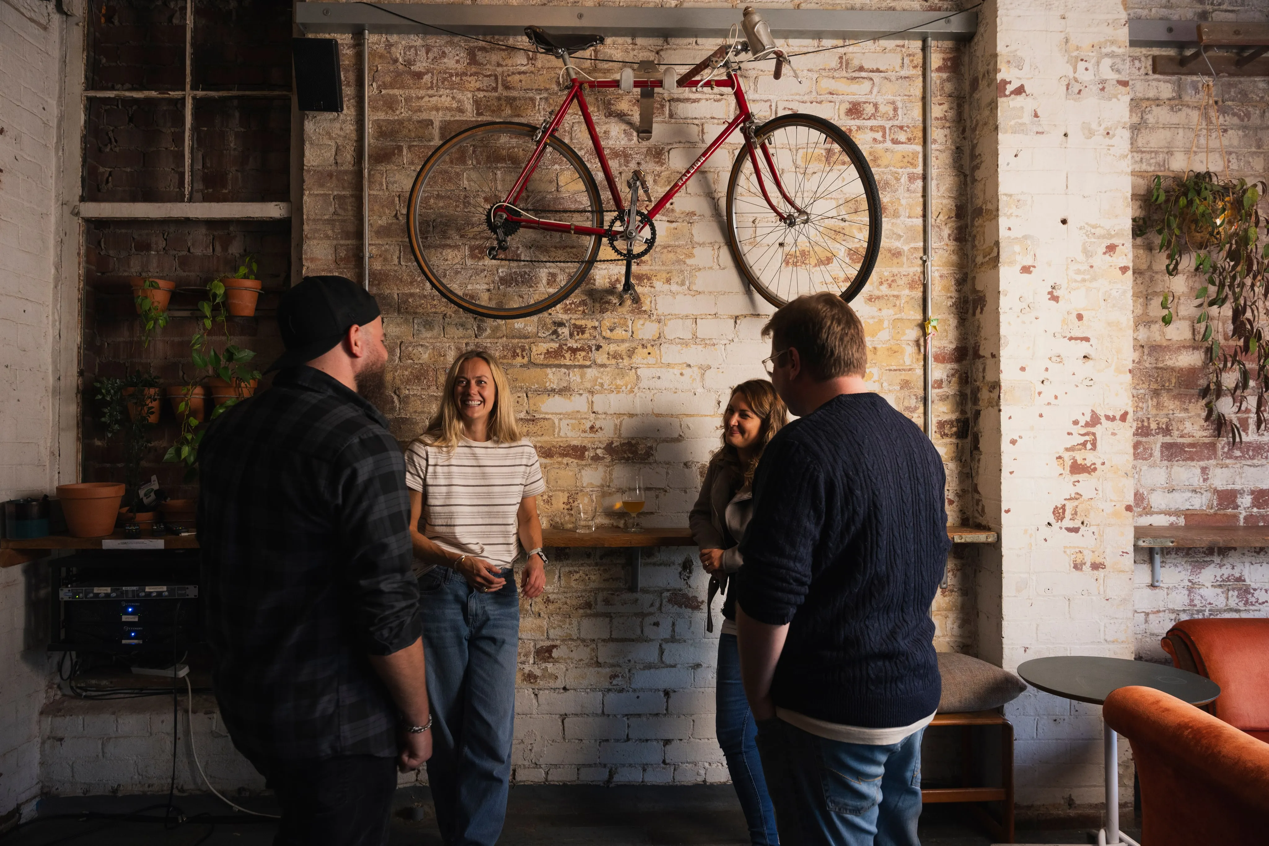 The team chatting in the Clubhouse, under bikes hung on a brick wall