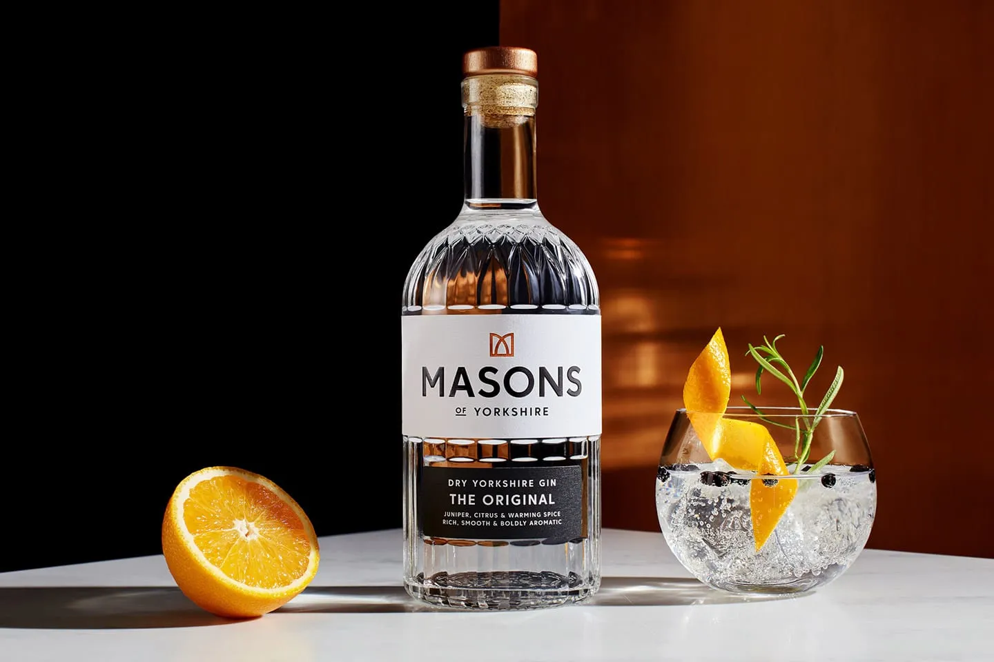 A bottle of Masons of Yorkshire gin beside a gin and tonic with orange
