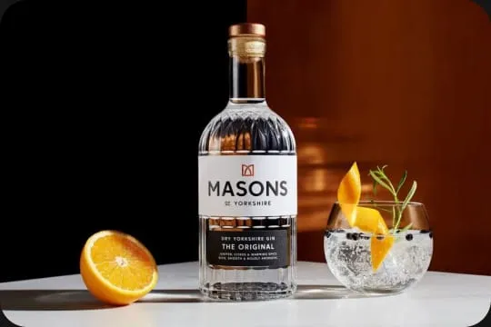 A bottle of Masons of Yorkshire gin beside a gin and tonic with orange