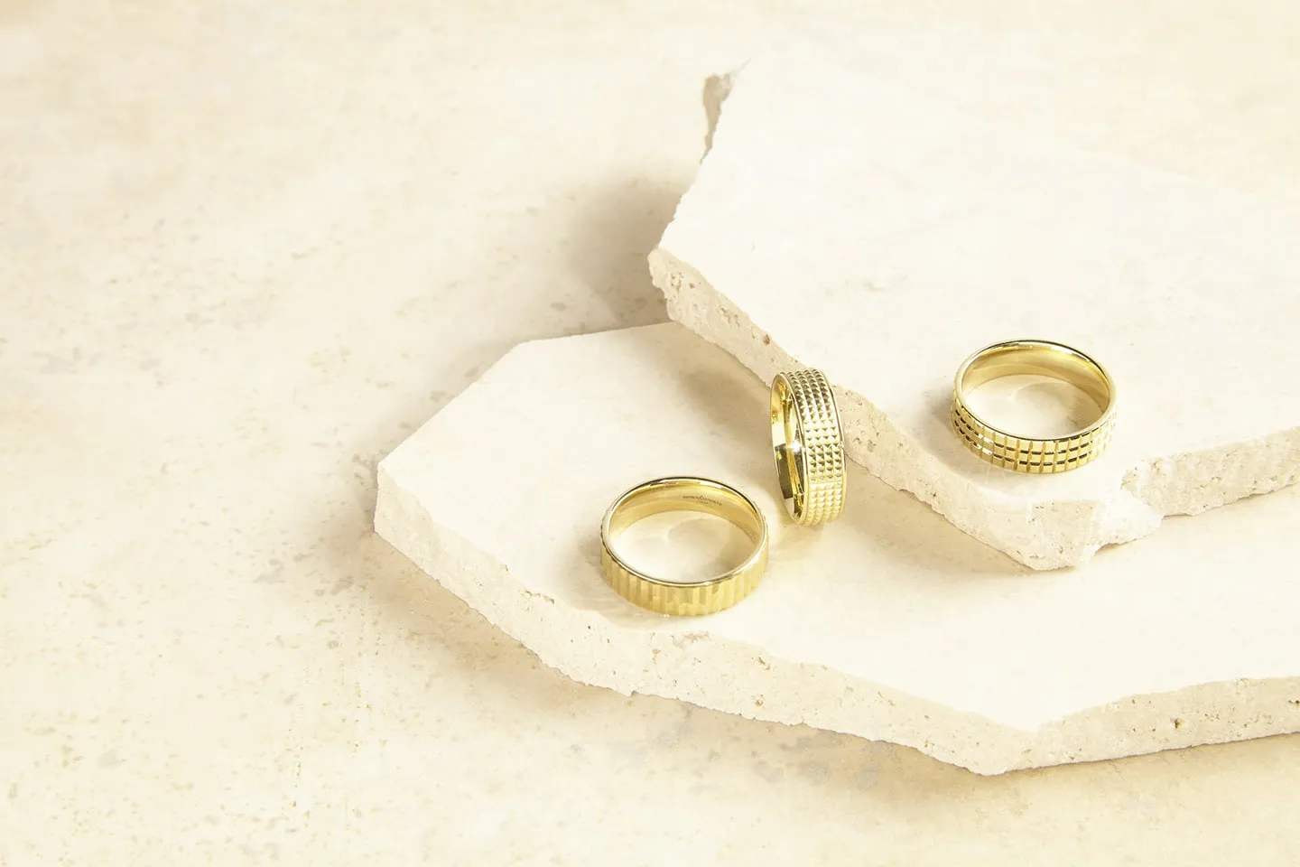 Two gold Brown & Newirth rings resting on a pale stone