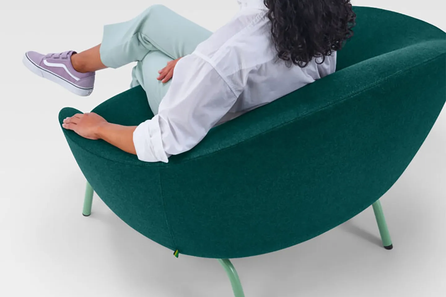 A woman sitting sideways in a green NaughtOne armchair