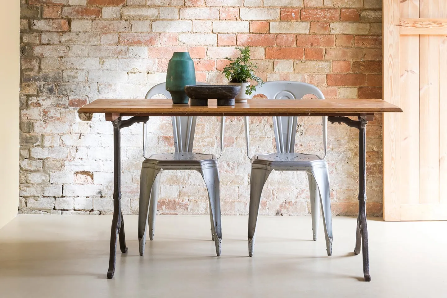 A vintage wooden table and metal chairs against a brick wall