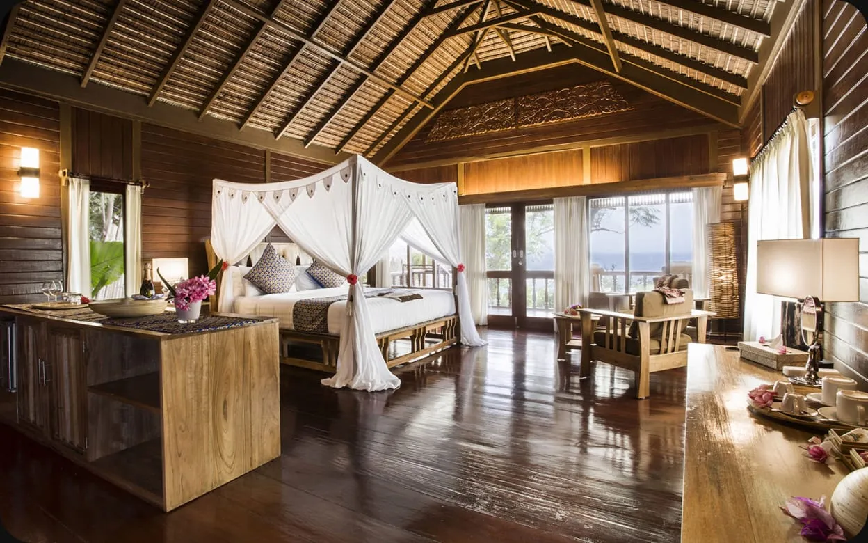A Bunaken Oasis villa bedroom with a four-poster bed and wooden floors