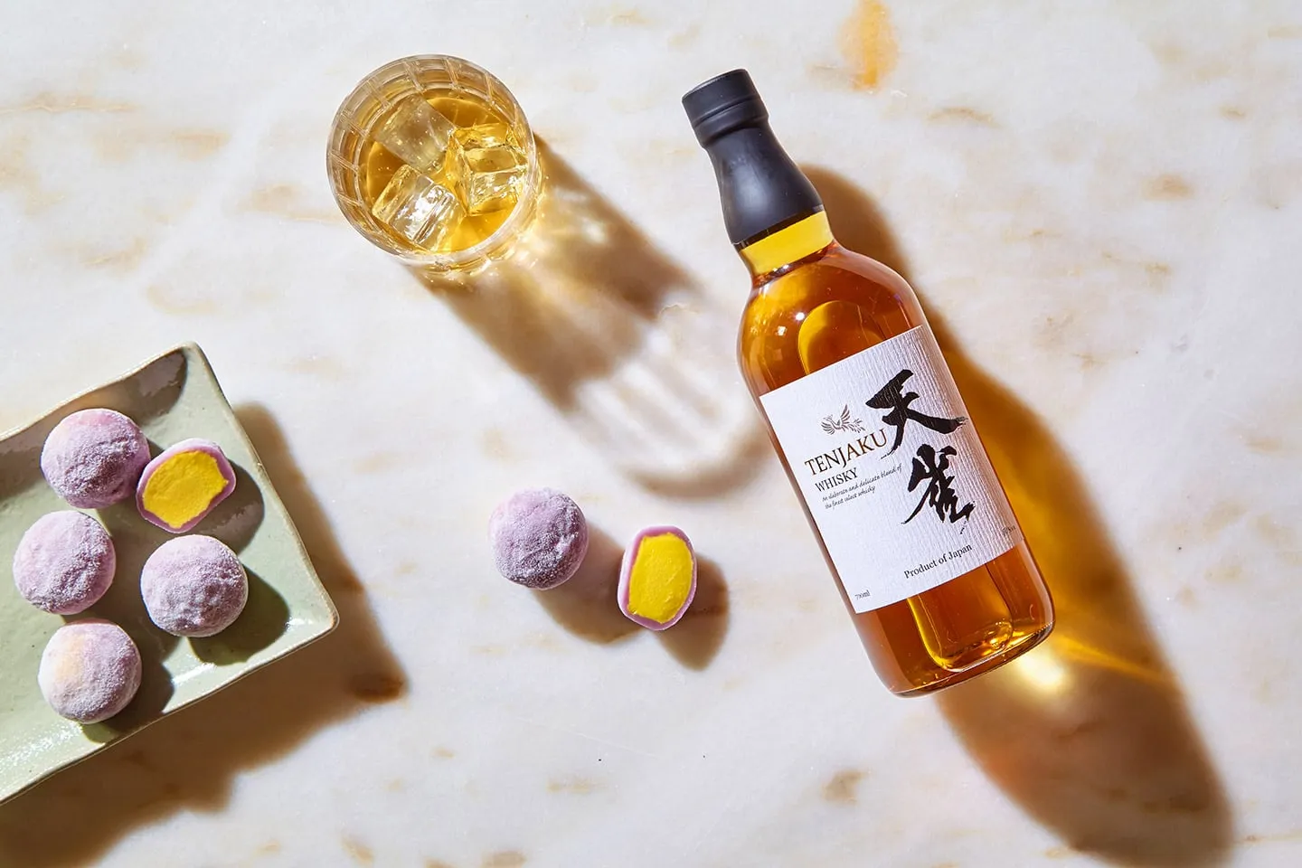 A bottle of Tenjaku and a glass of whisky beside lilac mochi