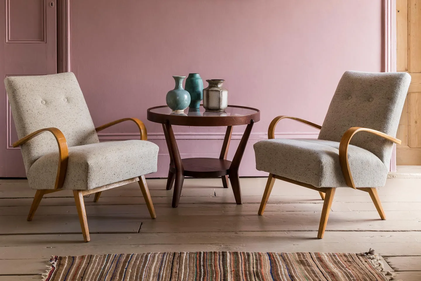 Two mid-century armchairs and a side table in a pink room
