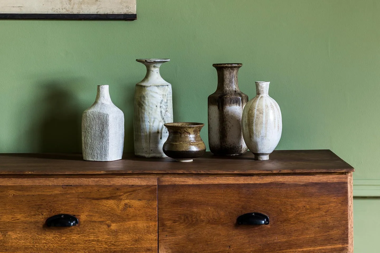 Vintage vases on a wooden sideboard against a green wall