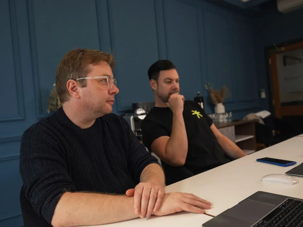Two of the team at a desk in the studio, one turning to listen