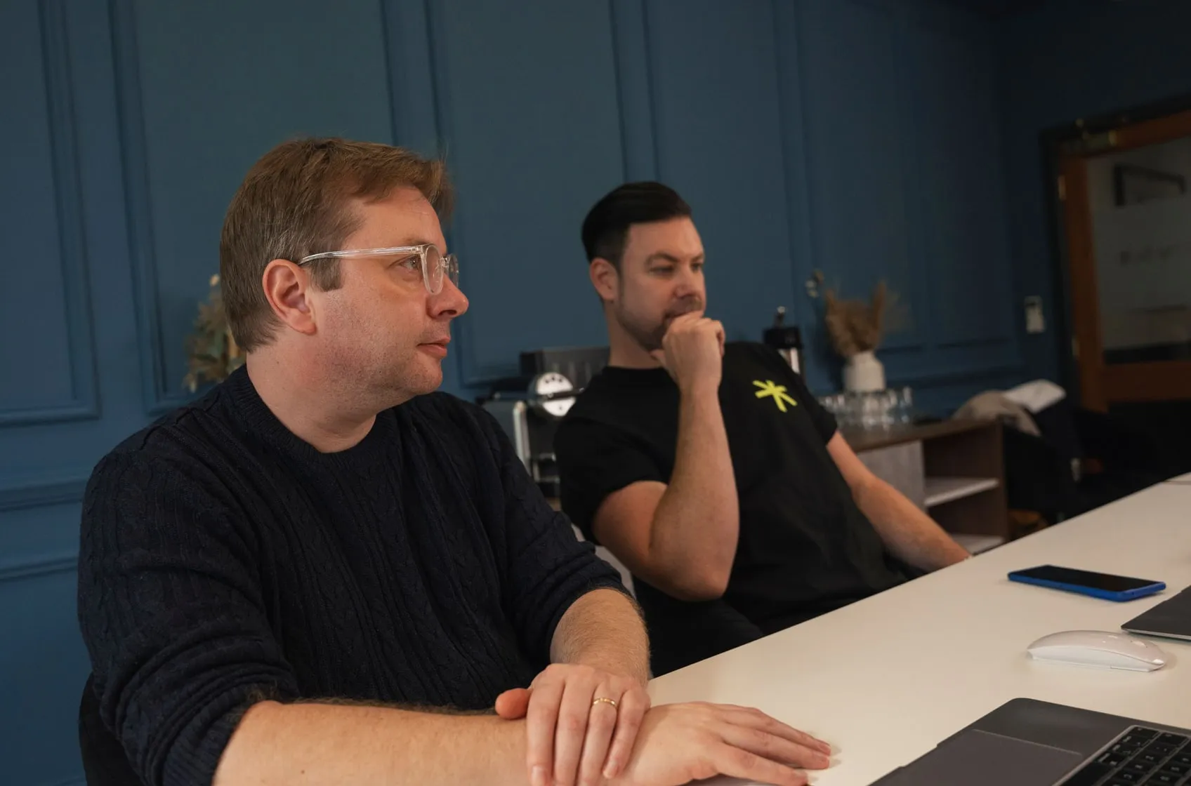 Two of the team at a desk in the studio, one turning to listen