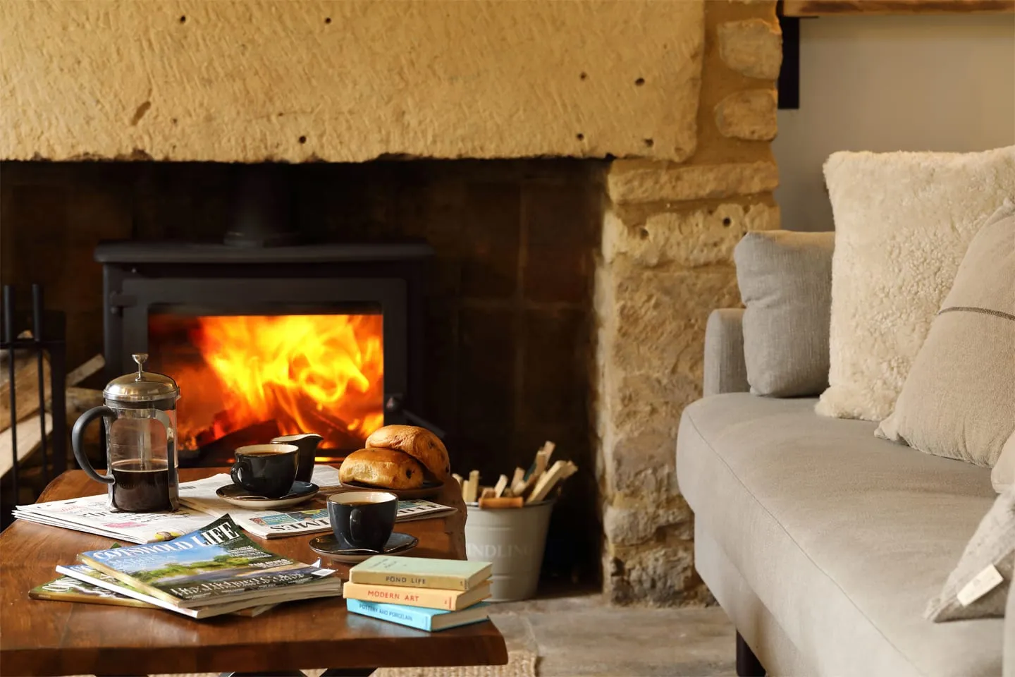 A wood-burning stove lit beside a table of books and coffee at The Feathered Nest