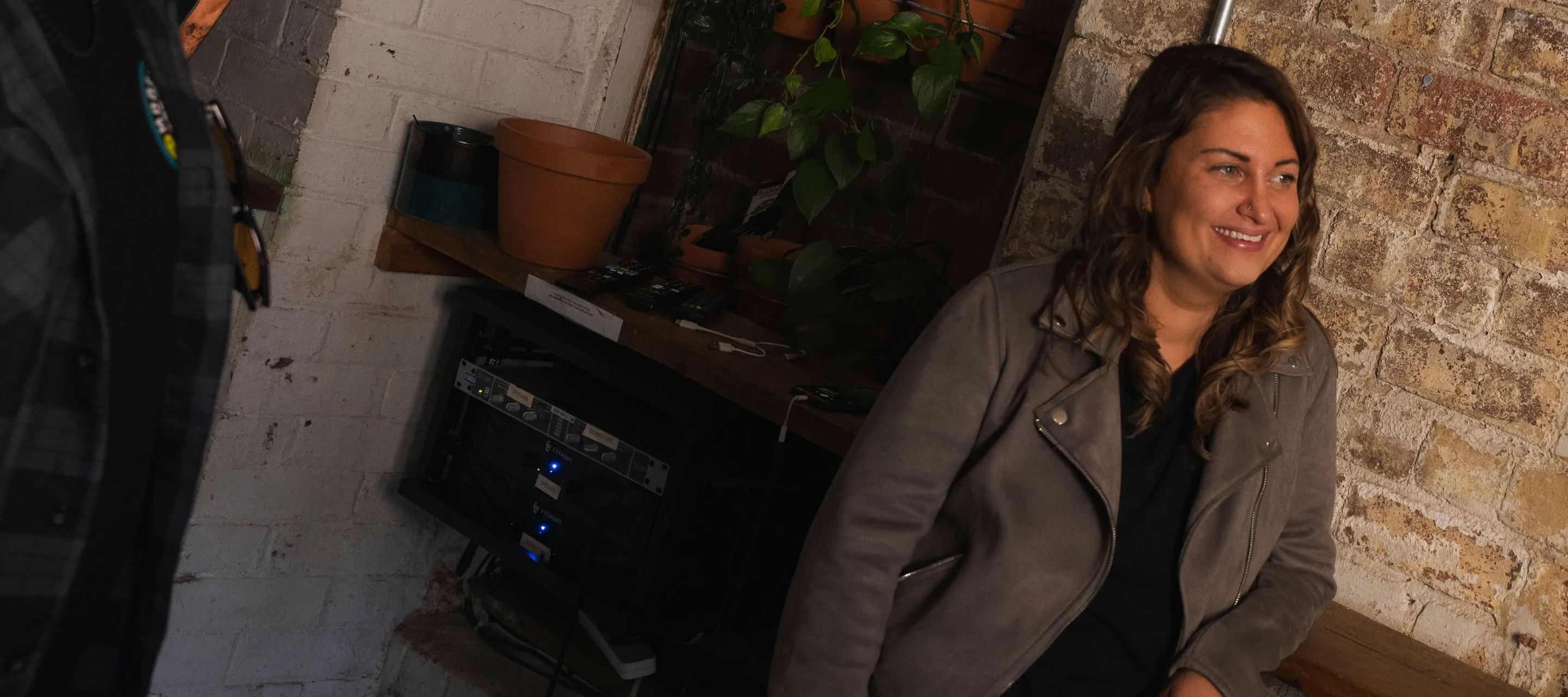 Vicqui James smiling, sitting by a brick wall in the studio